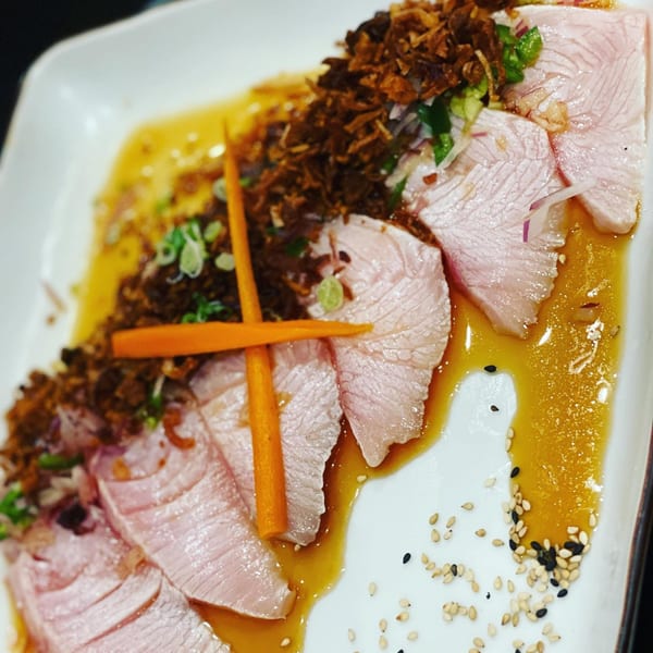 Seared tuna sashimi with crispy fried onions, green onions, and sesame seeds in a savory sauce.