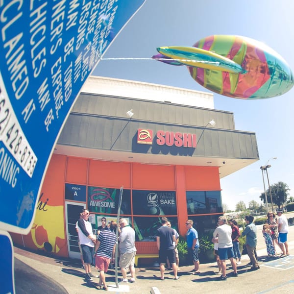 Awesome Sushi restaurant exterior with a colorful rocket balloon, people waiting outside, and a blue sign.