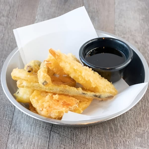 A metal bowl of golden-fried tempura, including shrimp and vegetables, with a side of dark dipping sauce.