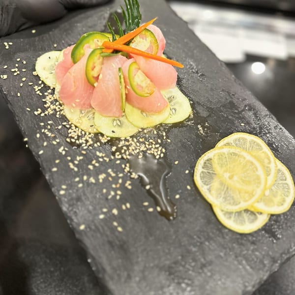 Awesome Sushi's tuna sashimi with jalapeños, carrots, and sesame seeds on a dark plate.