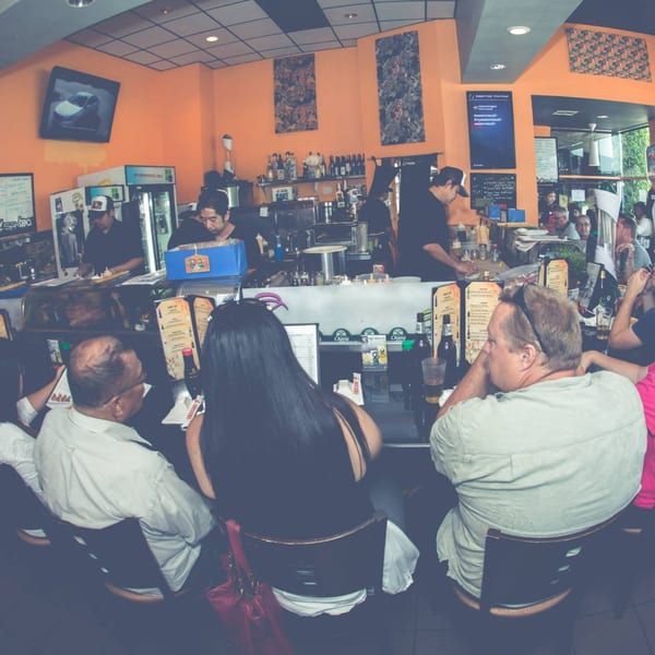 Diners seated at the sushi bar of Awesome Sushi, with chefs preparing food in the background.