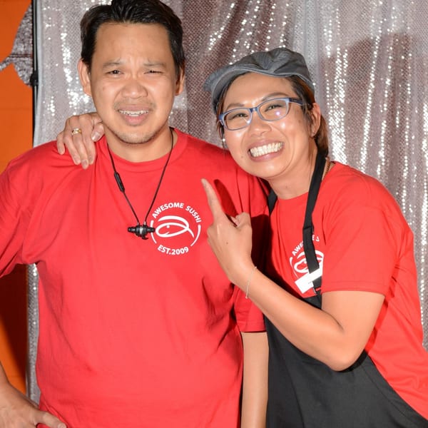 Two smiling Awesome Sushi staff members in red shirts, one pointing at the other's shirt.