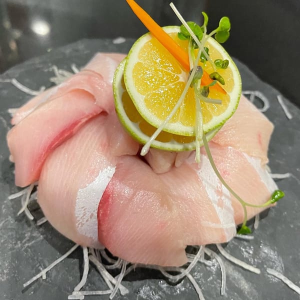 Awesome Sushi's yellowtail sashimi with citrus slices, microgreens, and shredded daikon on a dark plate.