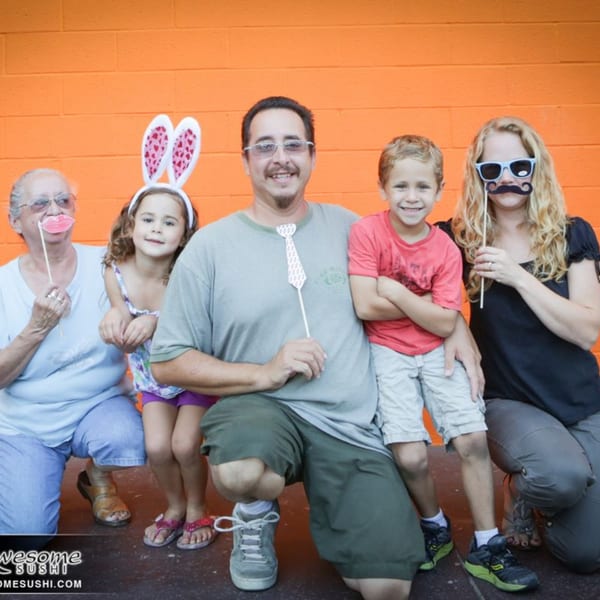 Five people, including children and adults, pose with fun props against an orange wall.
