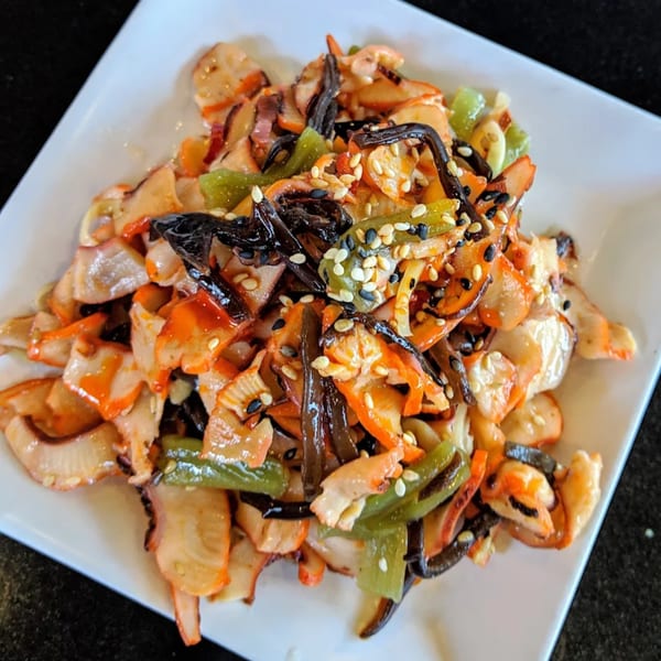 Awesome Sushi's Japanese octopus salad with green peppers, seaweed, and sesame seeds on a white plate.