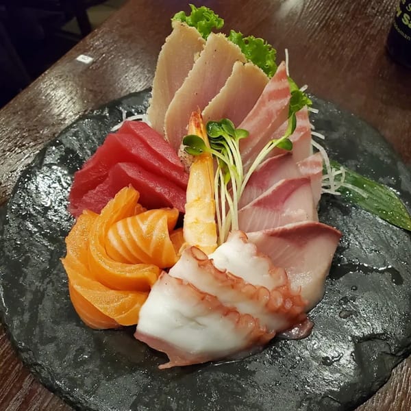 A colorful sashimi platter with tuna, salmon, octopus, shrimp, and other fish on a dark plate.