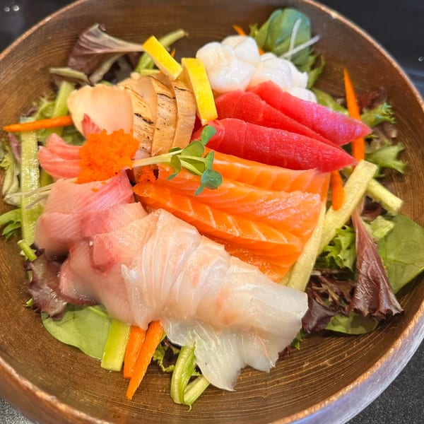 A wooden bowl filled with a colorful Awesome Sushi sashimi salad, featuring various fish, roe, and vegetables.