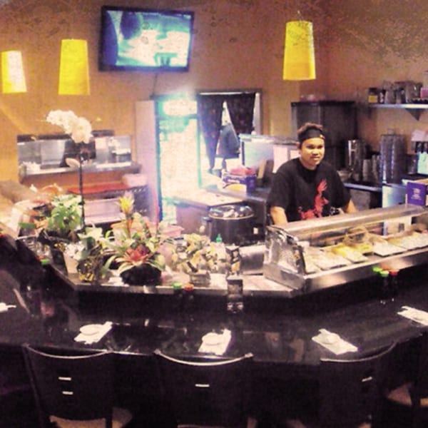 A sushi chef stands behind a counter filled with sushi rolls at Awesome Sushi.