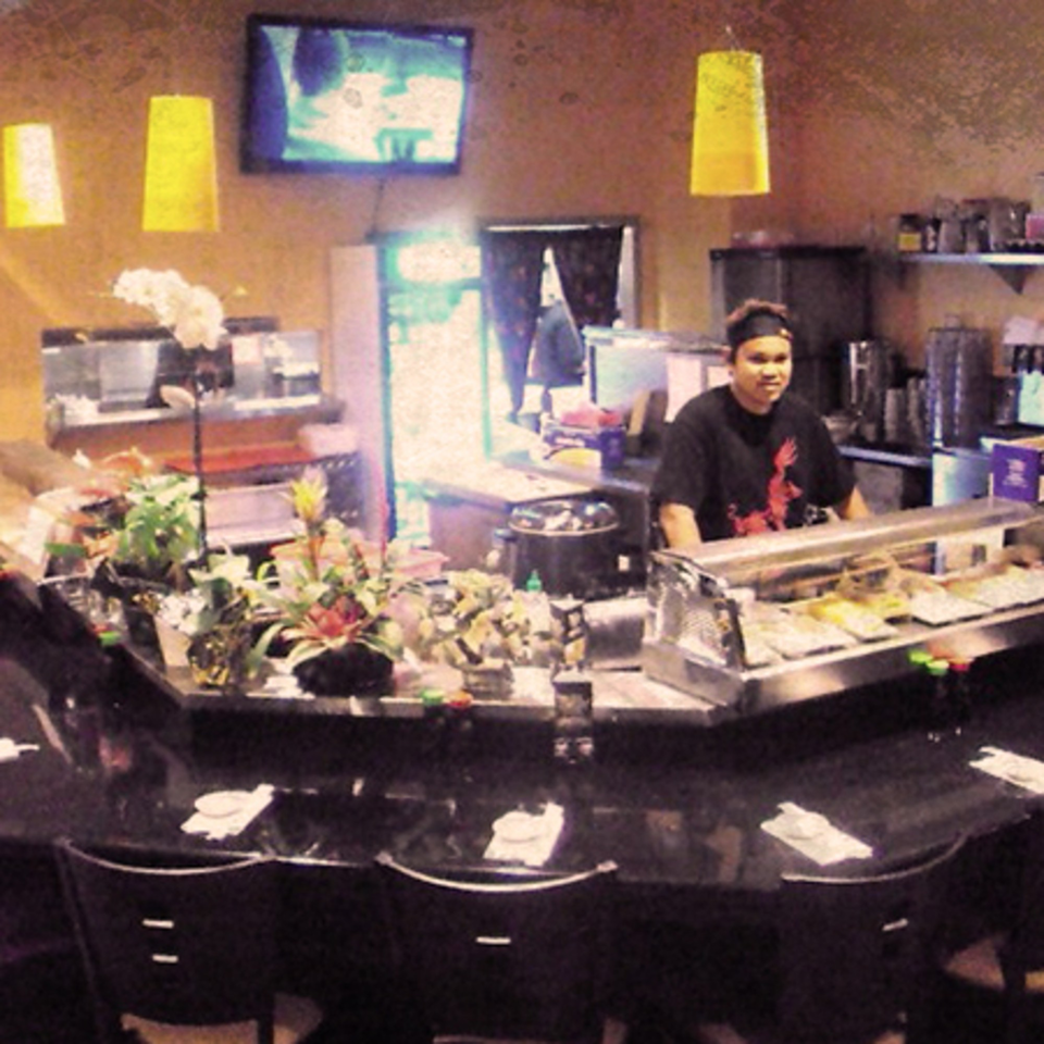 A sushi chef stands behind a counter filled with sushi rolls at Awesome Sushi.