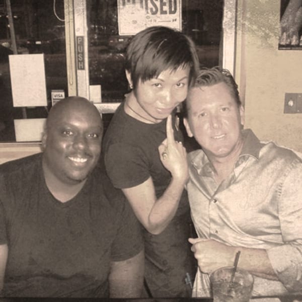 Three smiling people posing for a photo at Awesome Sushi, with one person pointing playfully.