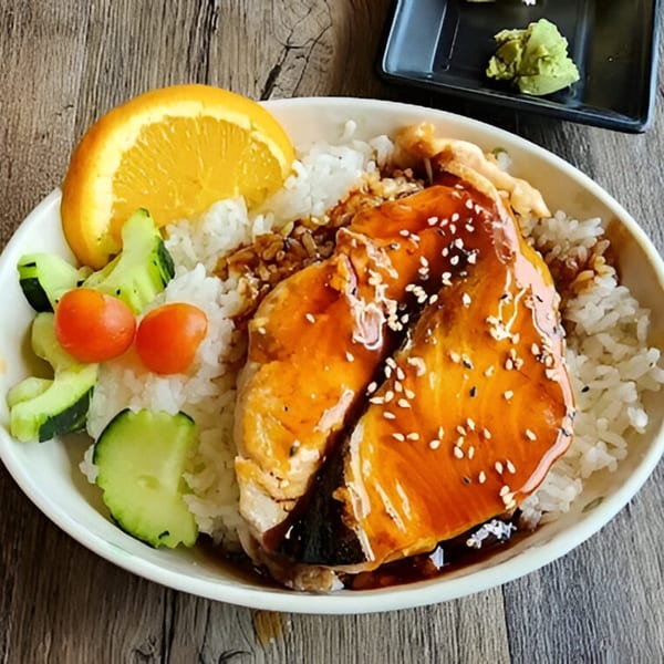 Awesome Sushi's teriyaki salmon over rice, with cucumber, cherry tomatoes, and an orange slice.