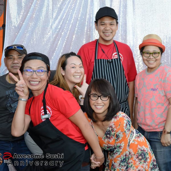 Six smiling Awesome Sushi staff members pose together in front of a sparkly white backdrop.
